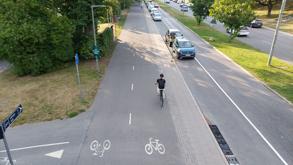 Bred dubbelfilig cykelbana sedd ur fågelperspektiv, med gott om plats för cyklister, längs en avsmalnad bilgata.